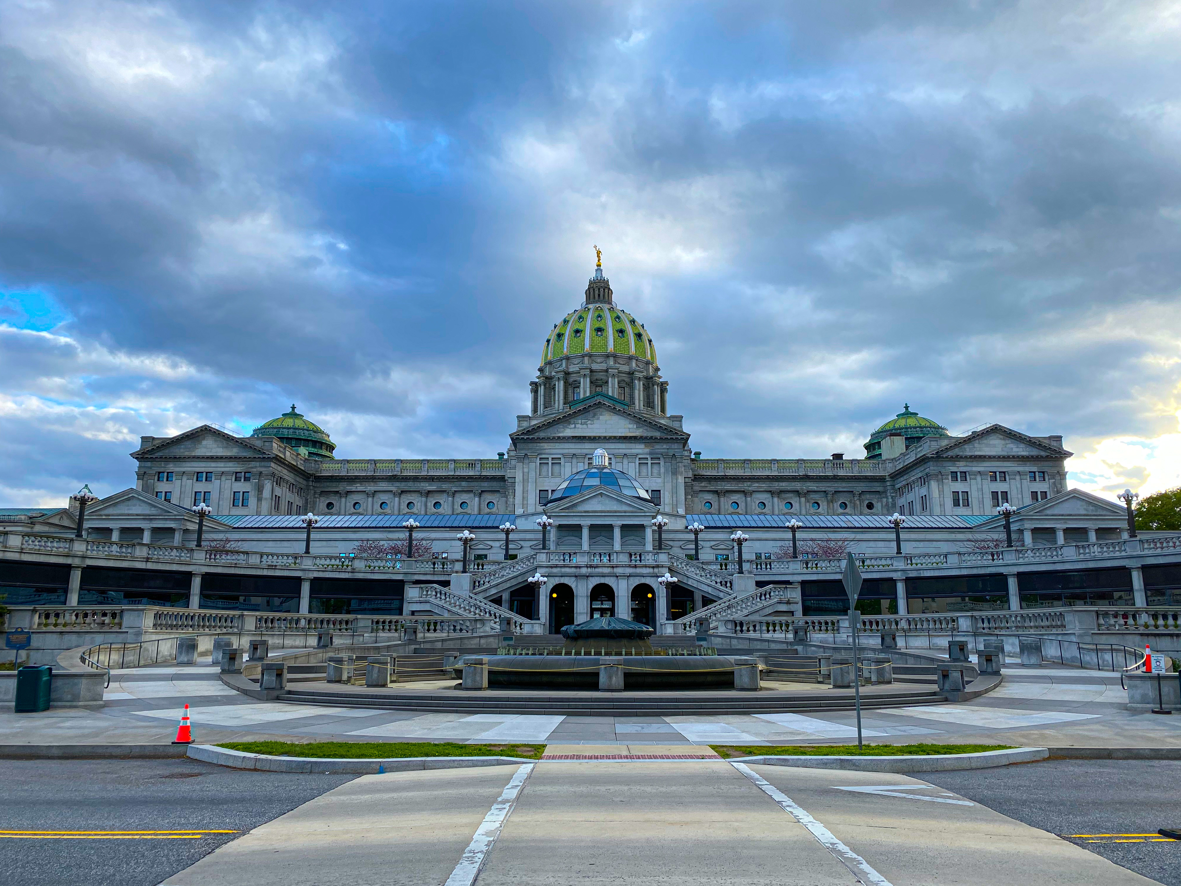 East side of the Pennsylvania State Capitol in Harrisburg, with its central green dome under a cloudy sky.